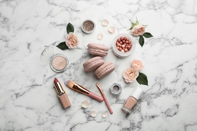 Flat lay composition with makeup products, roses and macarons on white marble background