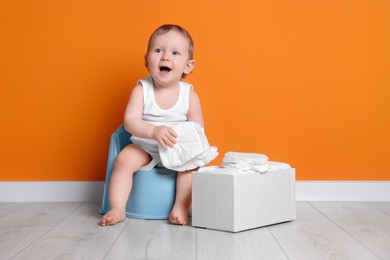 Little child sitting on baby potty and box of diapers near orange wall