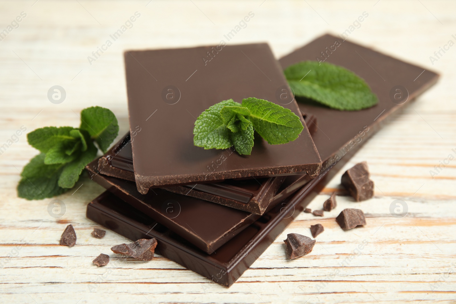 Photo of Tasty dark chocolate pieces with mint on white wooden table, closeup