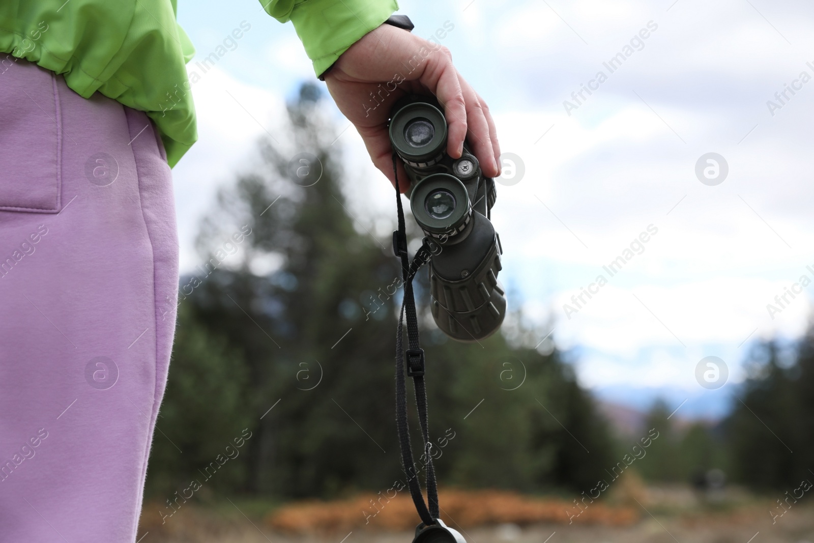 Photo of Woman holding binoculars in beautiful mountains, closeup. Space for text