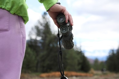 Woman holding binoculars in beautiful mountains, closeup. Space for text