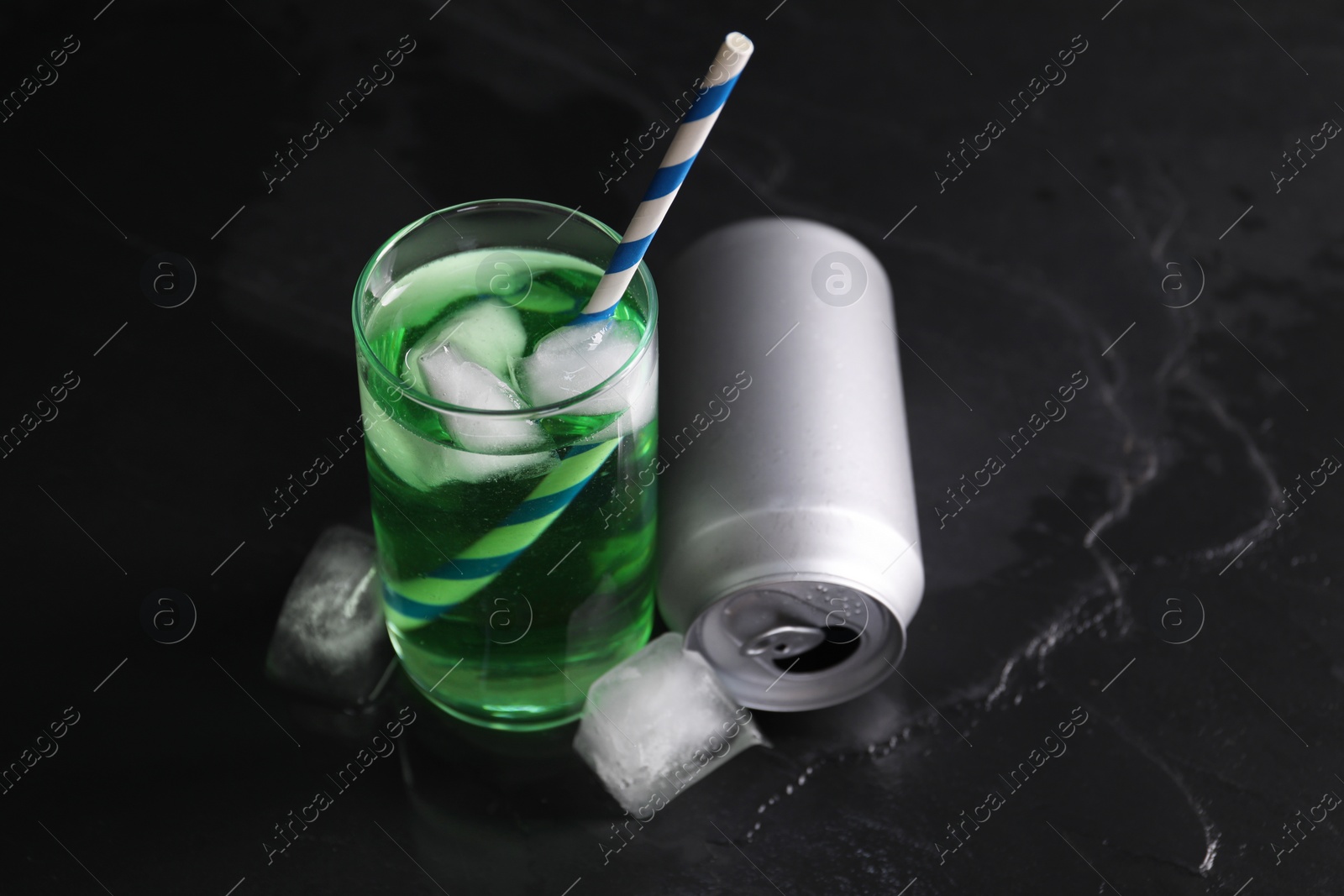 Photo of Tasty energy drink with ice cubes in glass and aluminium can on black table