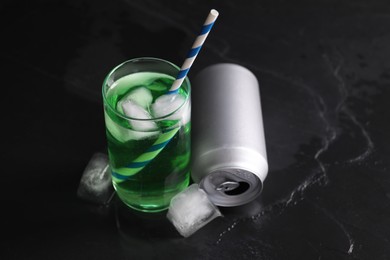 Photo of Tasty energy drink with ice cubes in glass and aluminium can on black table