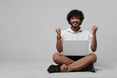 Emotional man with laptop on light grey background, space for text