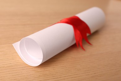 Photo of Graduation diploma tied with red ribbon on wooden table, closeup