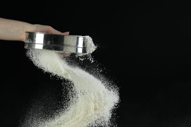 Woman sieving flour against black background, closeup. Space for text