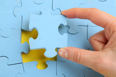 Woman putting light blue puzzle piece on yellow background, closeup. Career promotion concept