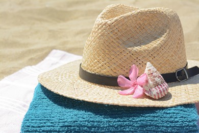 Photo of Stylish straw hat with flower, seashell on towel, closeup. Beach accessories