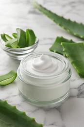 Jar with cream and cut aloe leaves on white marble table