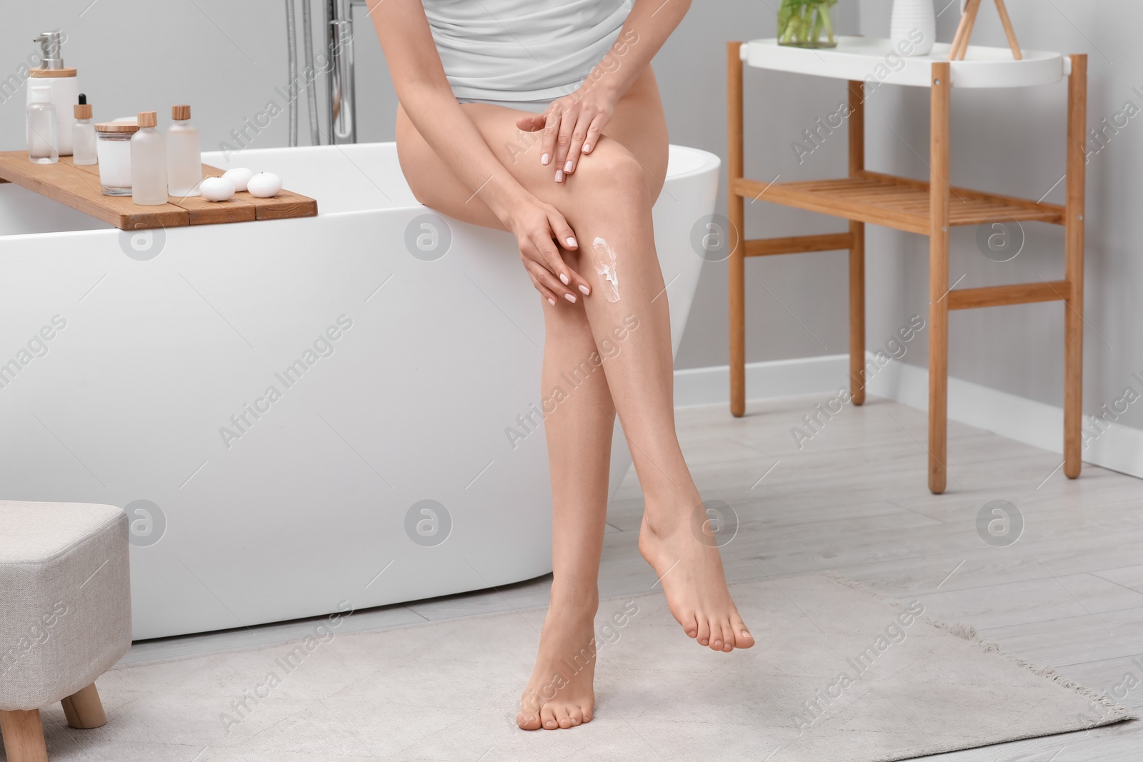 Photo of Woman applying body cream onto her smooth legs in bathroom, closeup