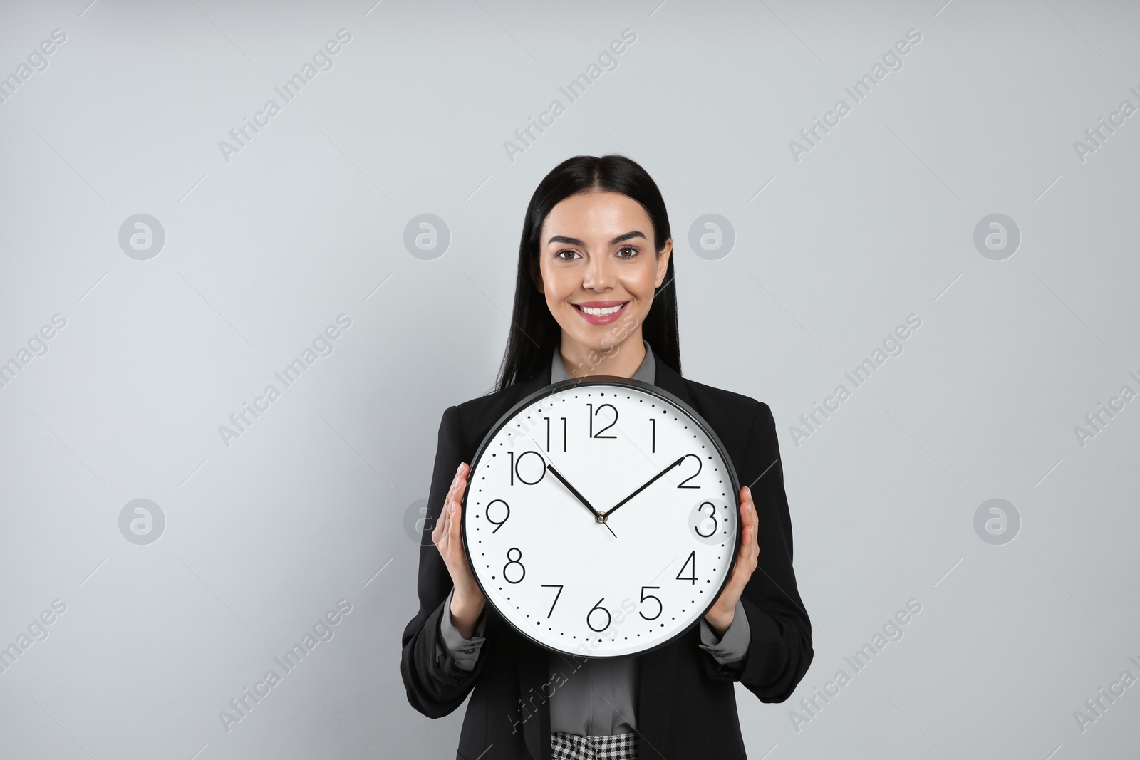 Photo of Businesswoman holding clock on light grey background. Time management