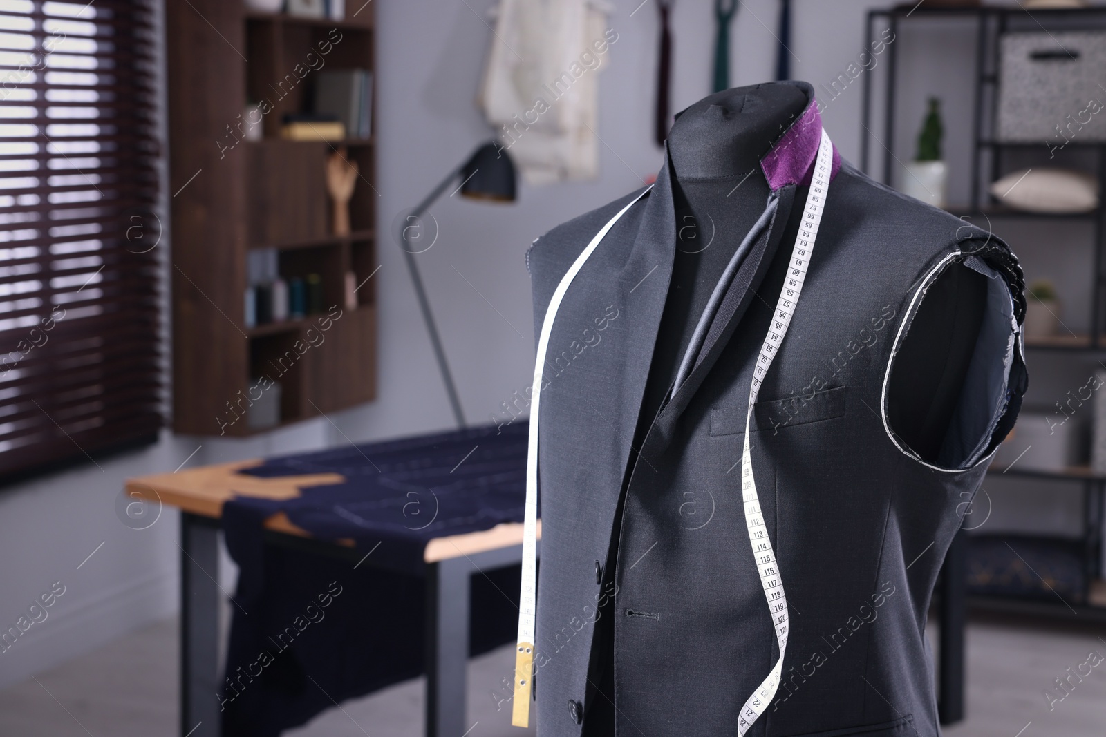 Photo of Mannequin with unfinished suit jacket and measuring tape in tailor shop, space for text