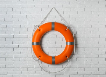 Photo of Orange lifebuoy on white brick wall. Rescue equipment