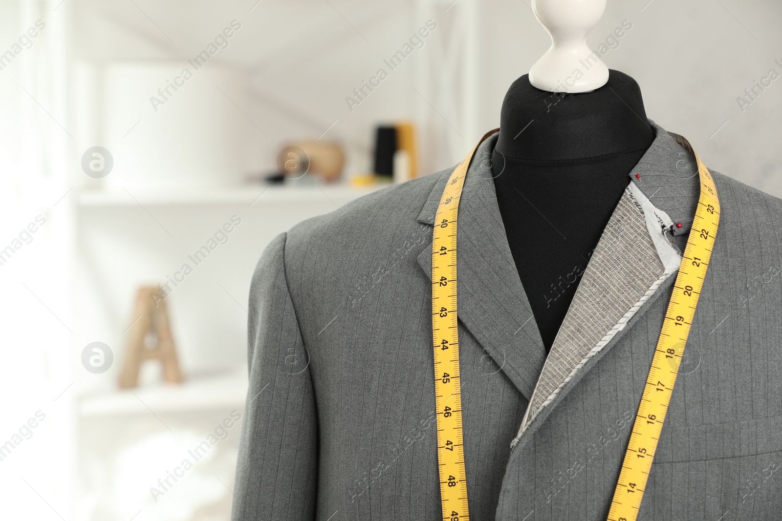 Photo of Mannequin with unfinished jacket and measuring tape in tailor shop, closeup. Space for text
