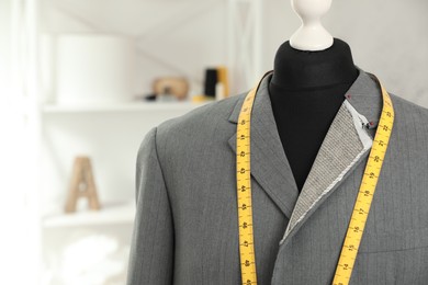 Photo of Mannequin with unfinished jacket and measuring tape in tailor shop, closeup. Space for text