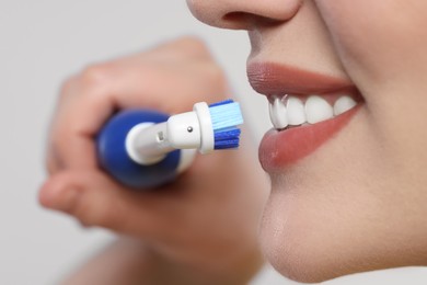 Woman brushing her teeth with electric toothbrush on white background, closeup