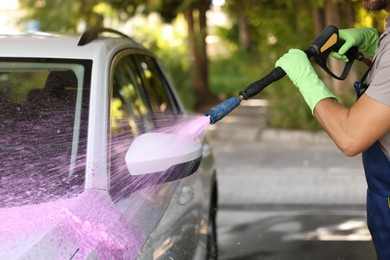 Worker washing auto with high pressure water jet at outdoor car wash, closeup
