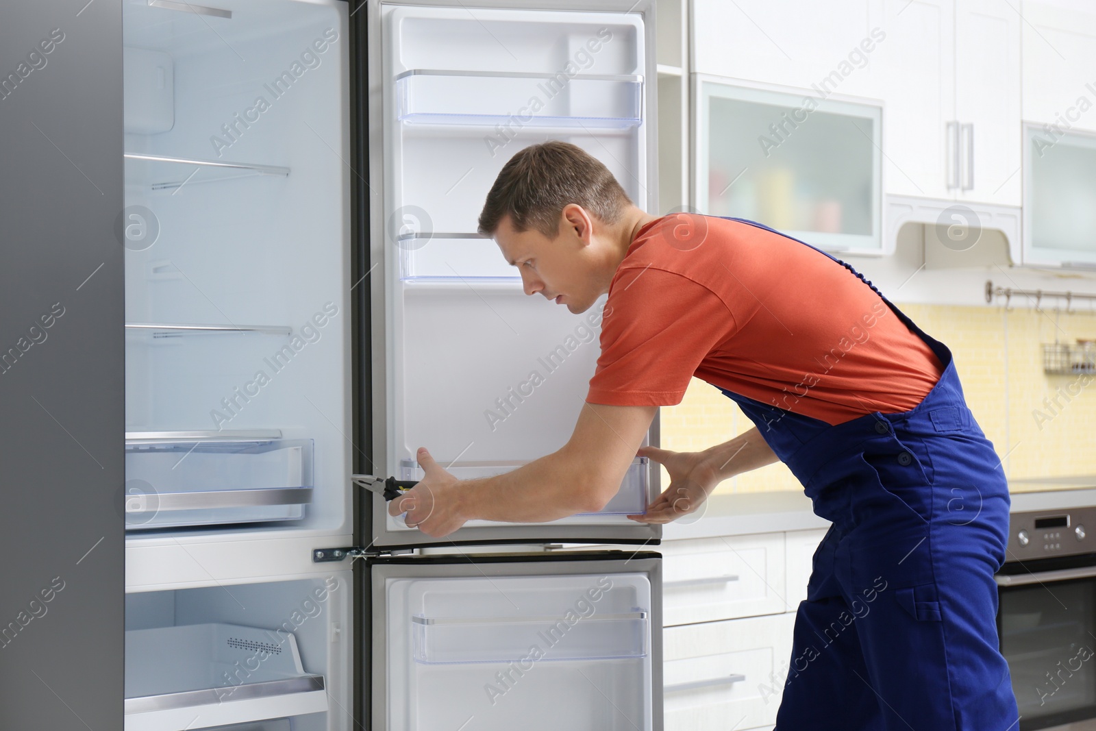 Photo of Male technician with pliers repairing refrigerator in kitchen
