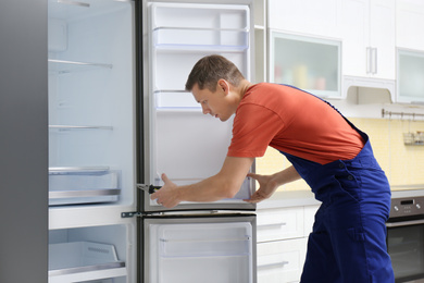 Male technician with pliers repairing refrigerator in kitchen