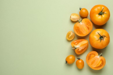 Photo of Cut and whole ripe yellow tomatoes on light green background, flat lay. Space for text