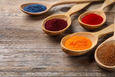 Photo of Many spoons with food coloring on wooden table, closeup. Space for text