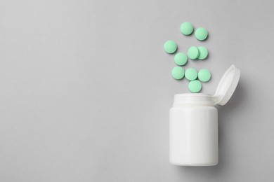 Light green vitamin pills and bottle on grey background, top view. Space for text