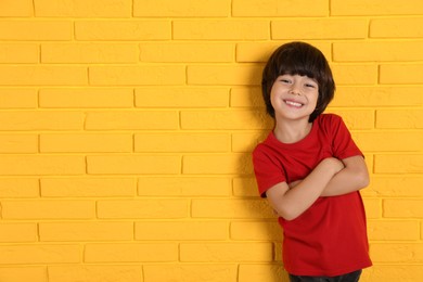 Photo of Cute little boy near yellow brick wall, space for text