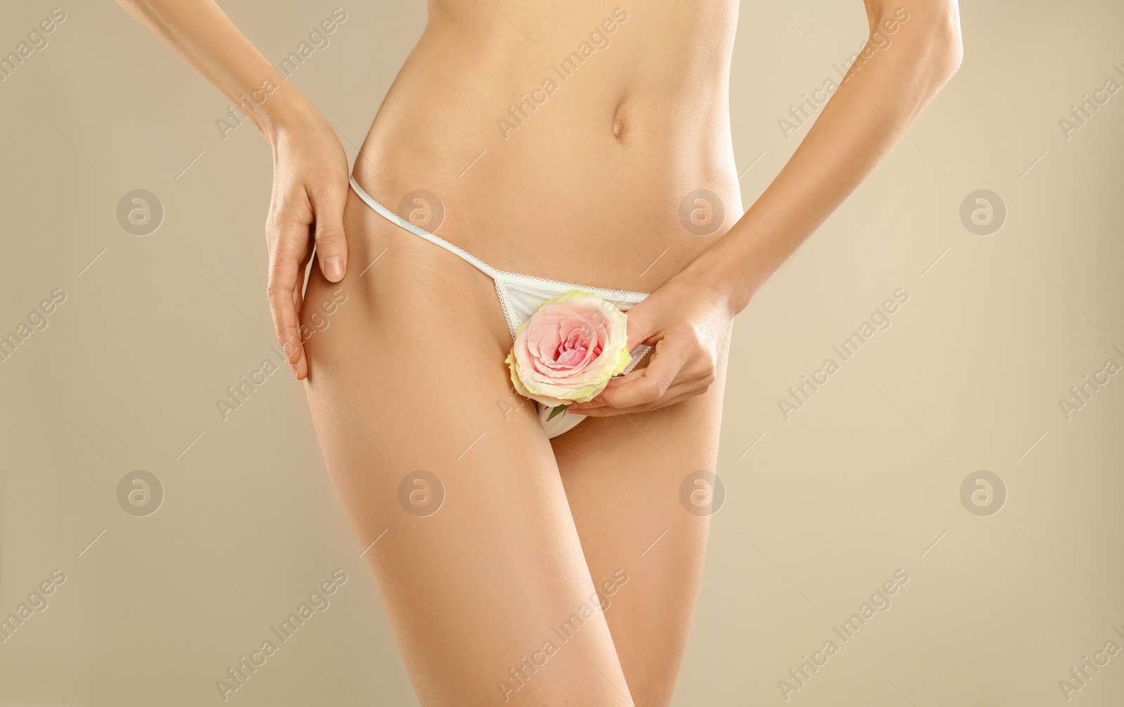 Photo of Woman with flower showing smooth skin after Brazilian bikini epilation on beige background, closeup. Body care concept