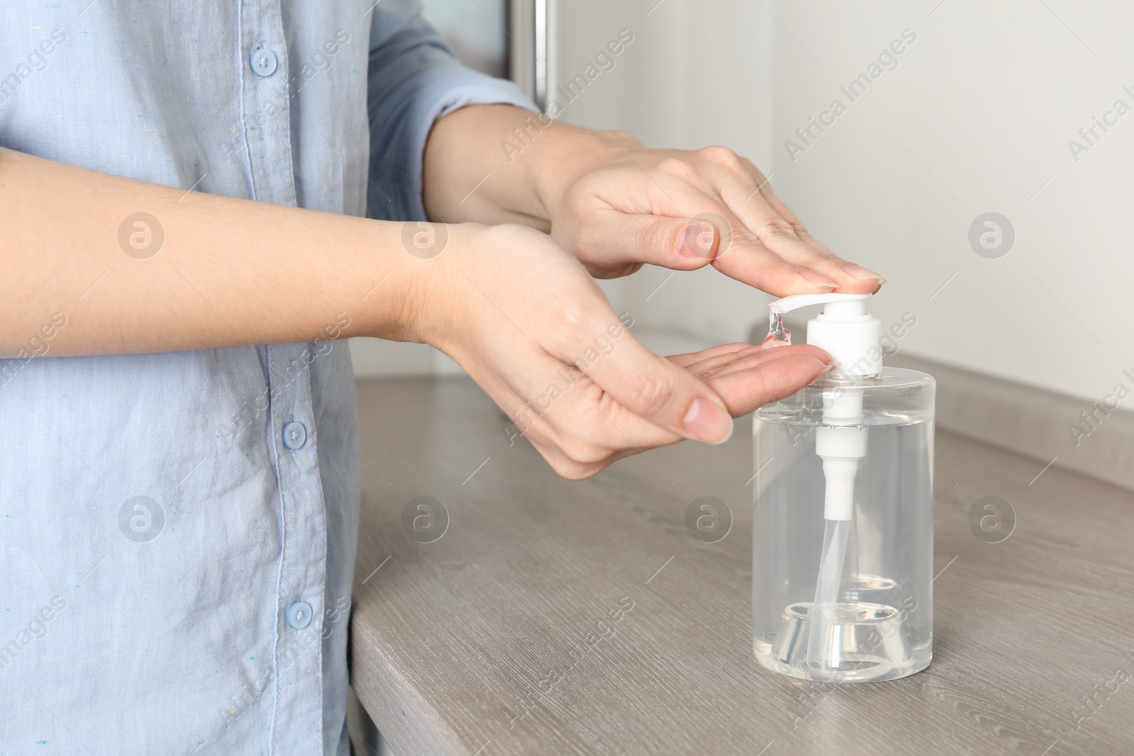 Photo of Woman applying antiseptic gel onto hand at table indoors, closeup. Virus prevention