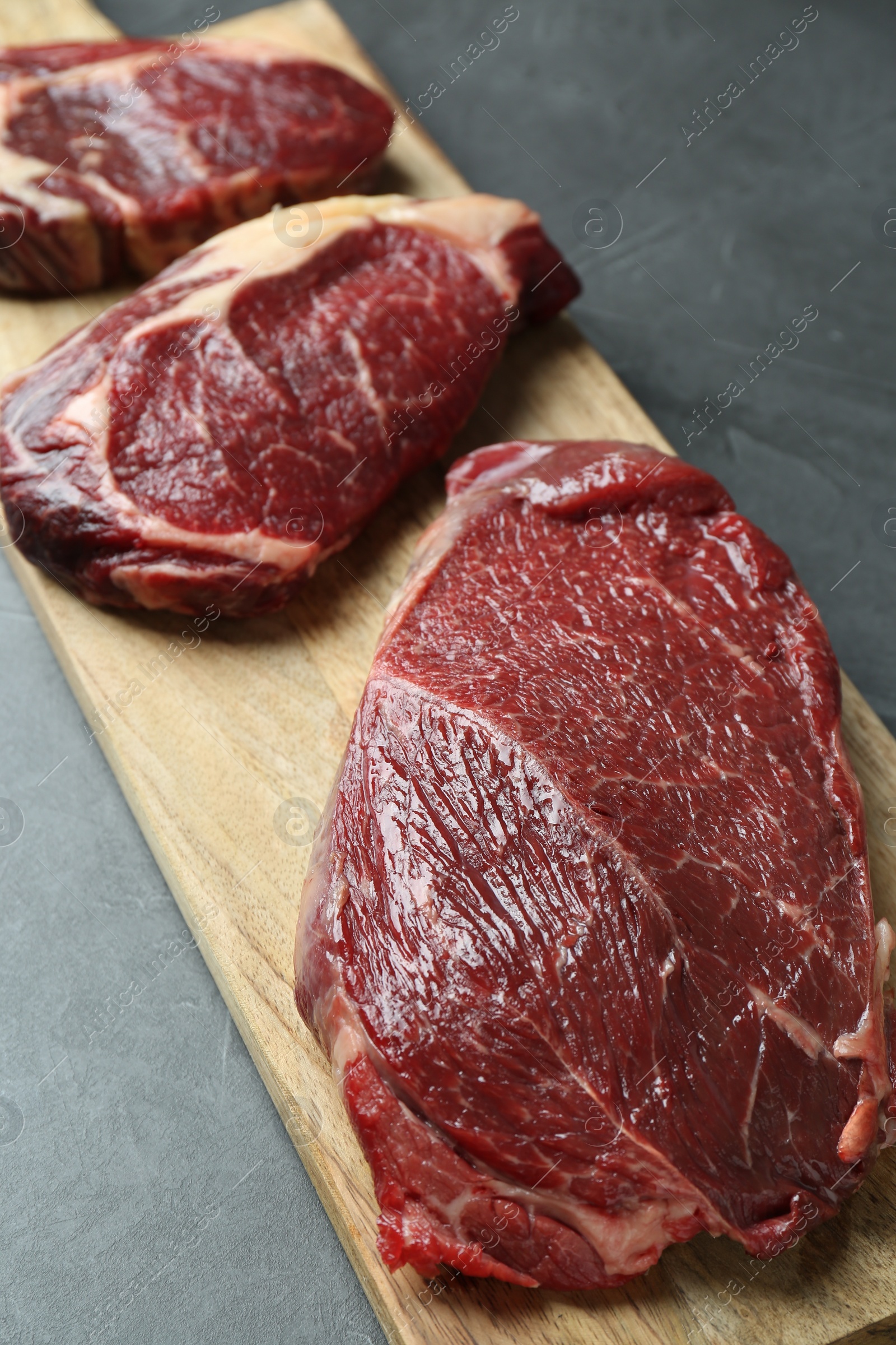 Photo of Wooden board with pieces of raw beef meat on grey table, closeup