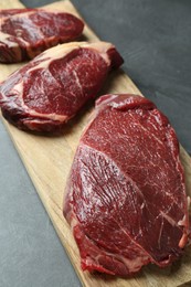 Wooden board with pieces of raw beef meat on grey table, closeup