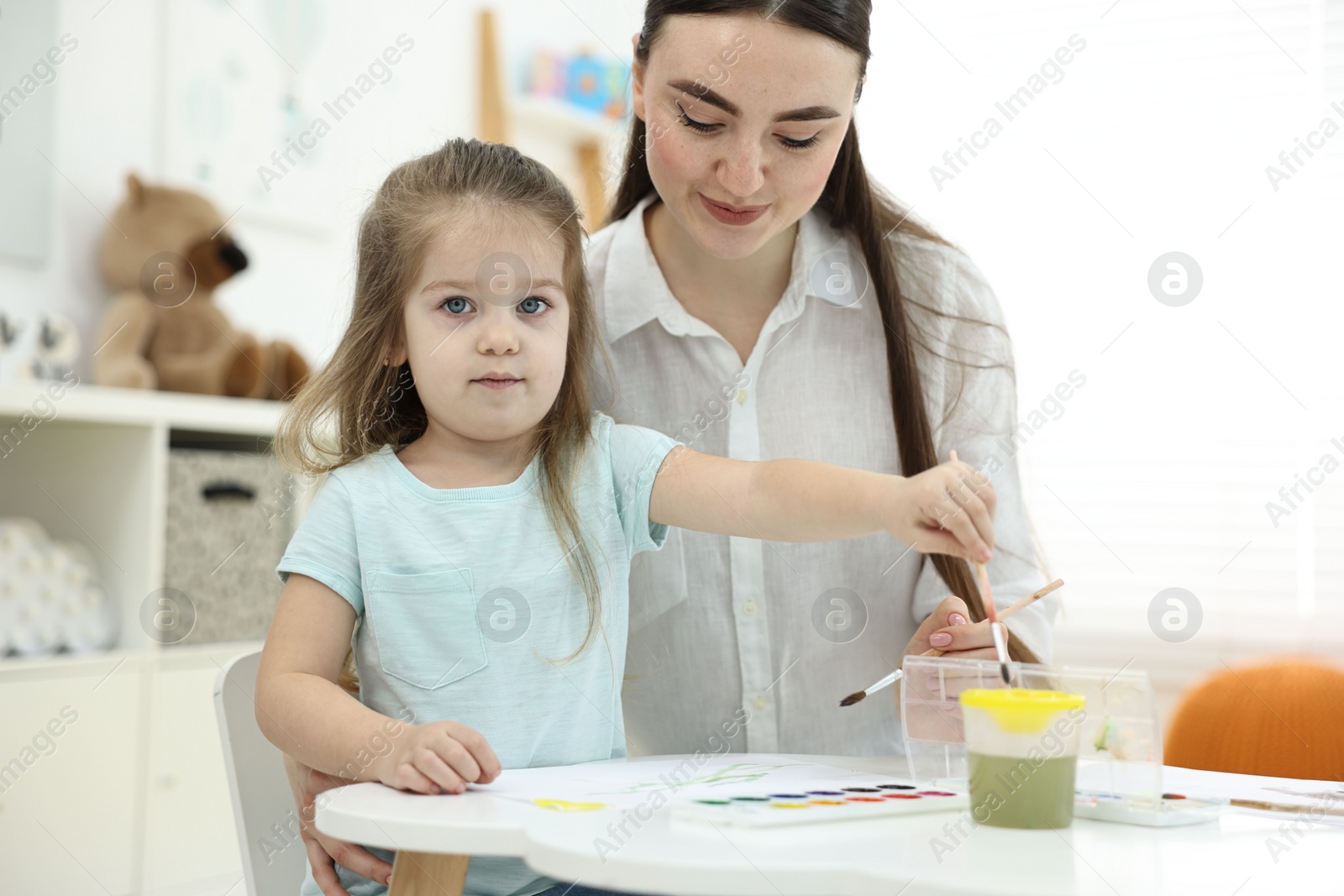 Photo of Mother and her little daughter painting with watercolor at home