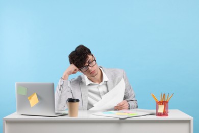Photo of Tired young man working at white table on light blue background. Deadline concept