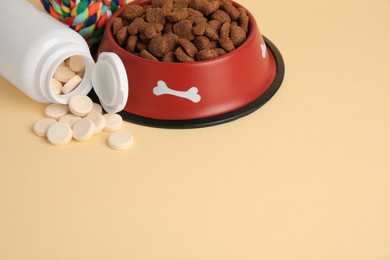 Photo of Bottle with vitamins, dry pet food in bowl and toy on beige background, space for text