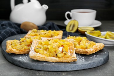 Fresh tasty puff pastry with sugar powder and kiwi on grey table, closeup