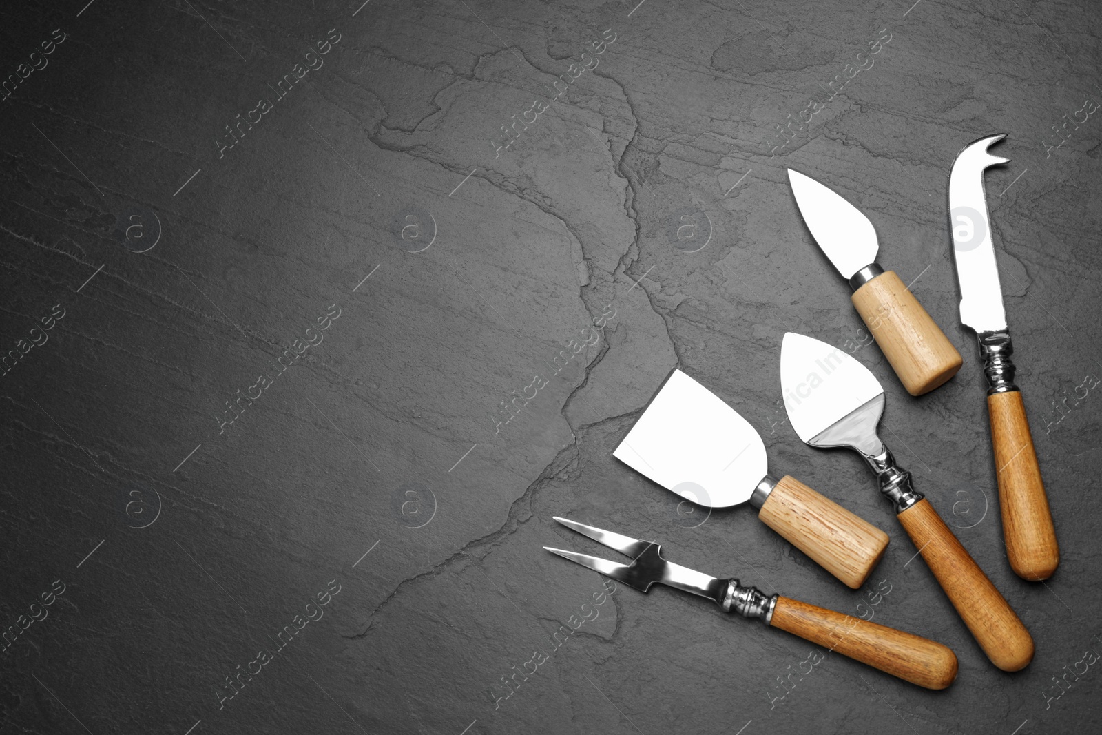 Photo of Cheese knives and fork on black stone table, flat lay. Space for text