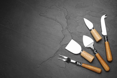 Photo of Cheese knives and fork on black stone table, flat lay. Space for text