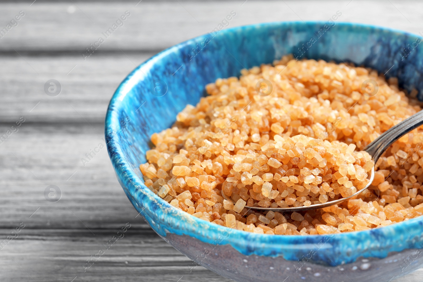 Photo of Spoon with brown sugar in bowl on table, closeup