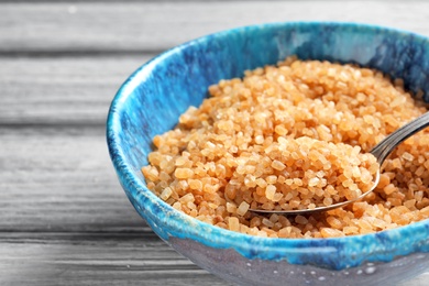 Spoon with brown sugar in bowl on table, closeup