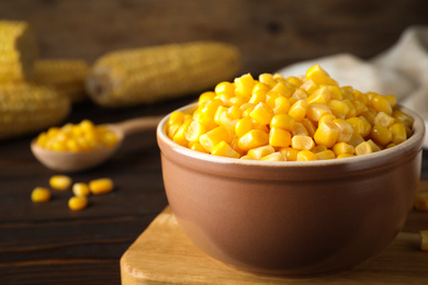 Photo of Delicious canned corn in bowl on wooden table, closeup