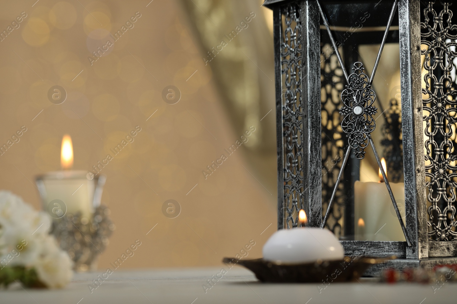 Photo of Arabic lantern and burning candles on table against blurred lights