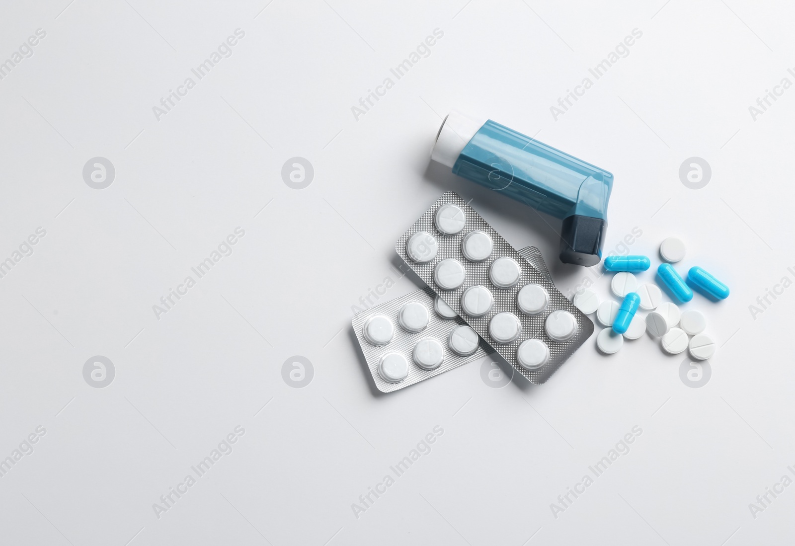 Photo of Asthma inhaler, pills and space for text on white background, top view