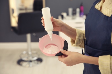 Professional hairdresser preparing dye for hair coloring in beauty salon, closeup