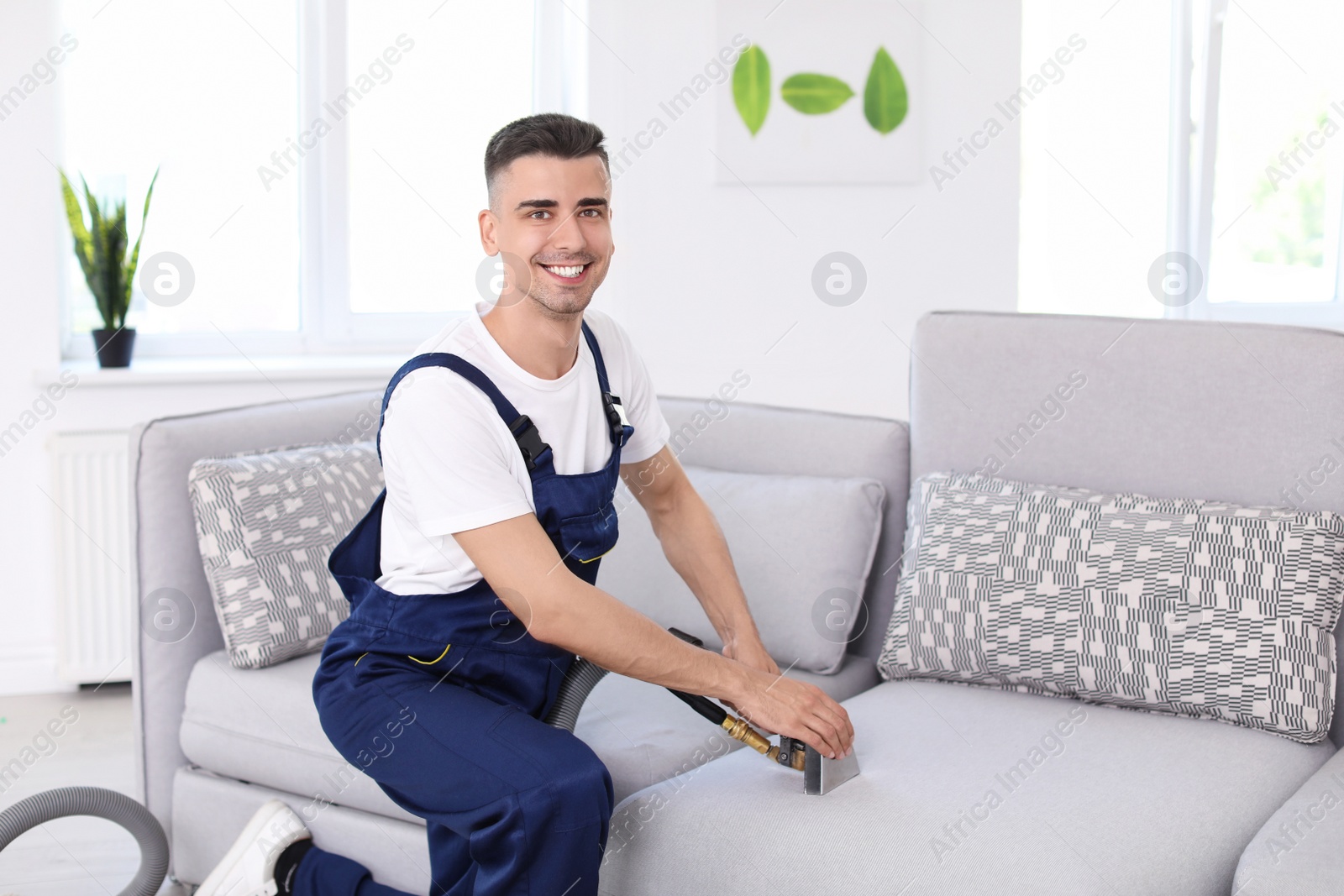 Photo of Dry cleaning worker removing dirt from sofa indoors