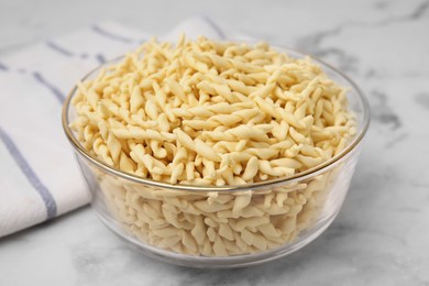 Photo of Uncooked trofie pasta in bowl on white marble table, closeup