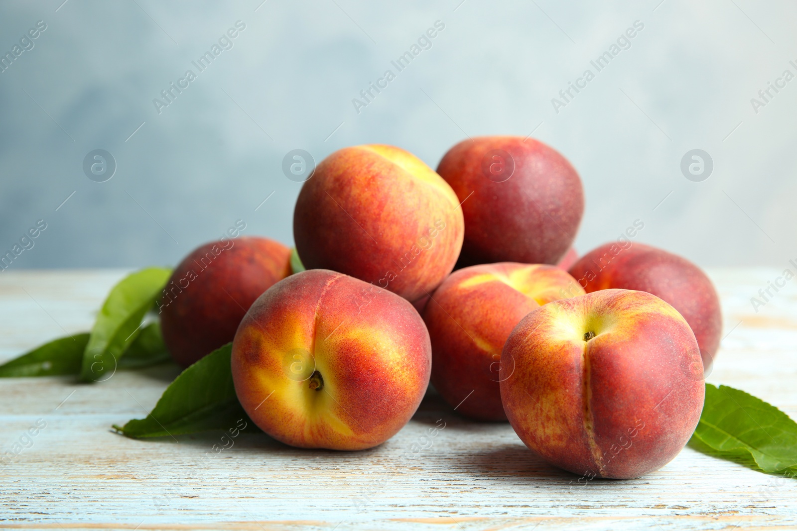 Photo of Fresh juicy peaches and leaves on wooden table against blue background