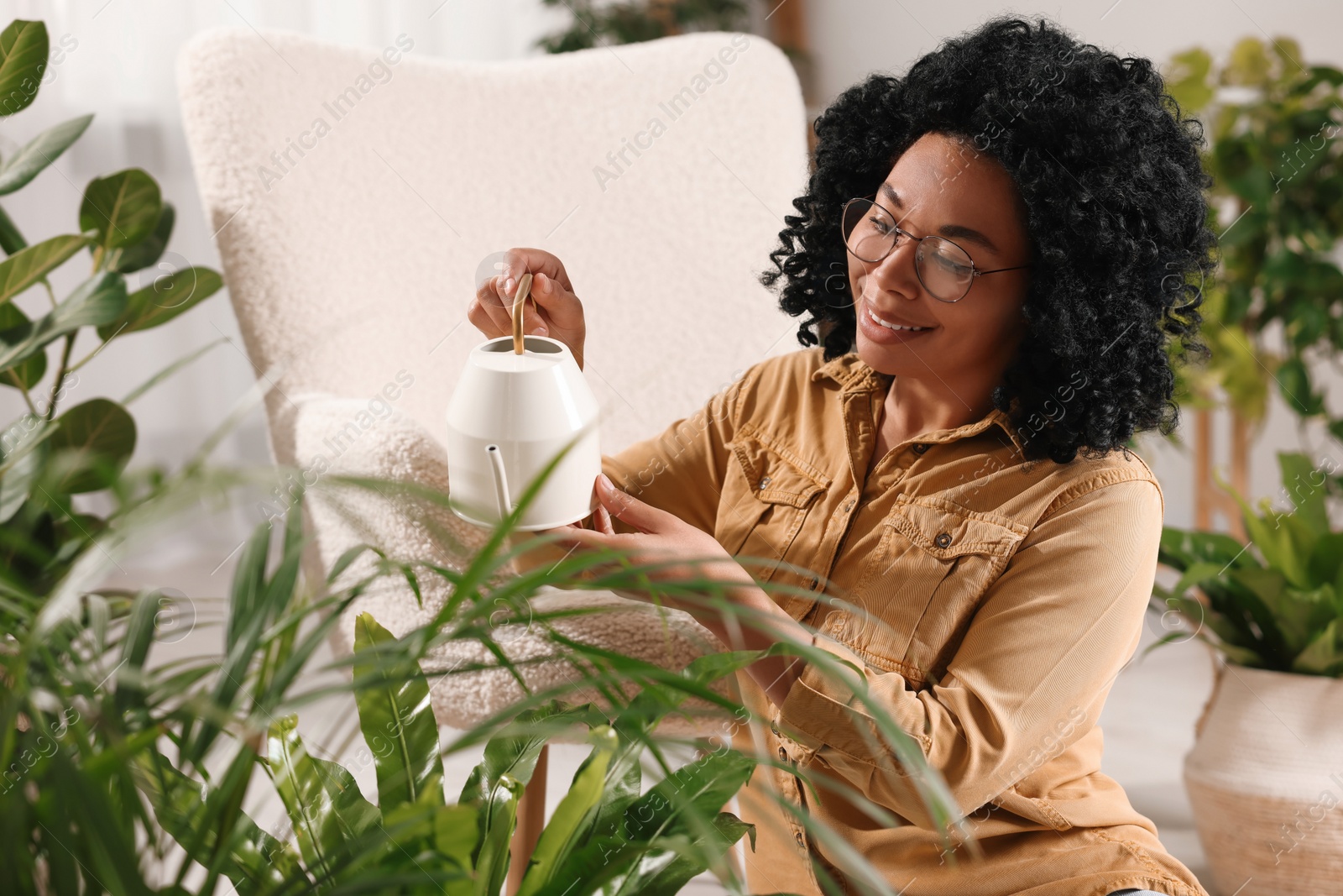 Photo of Happy woman watering beautiful houseplants at home