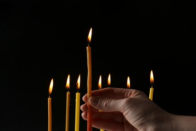 Woman holding burning church candle on black background, closeup