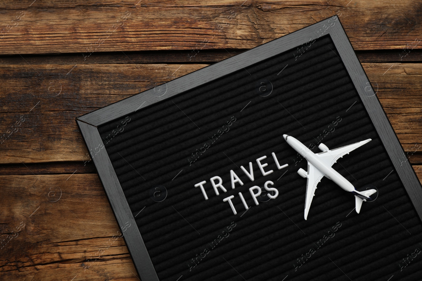 Photo of Black letter board with phrase Travel Tips and toy plane on wooden table, top view