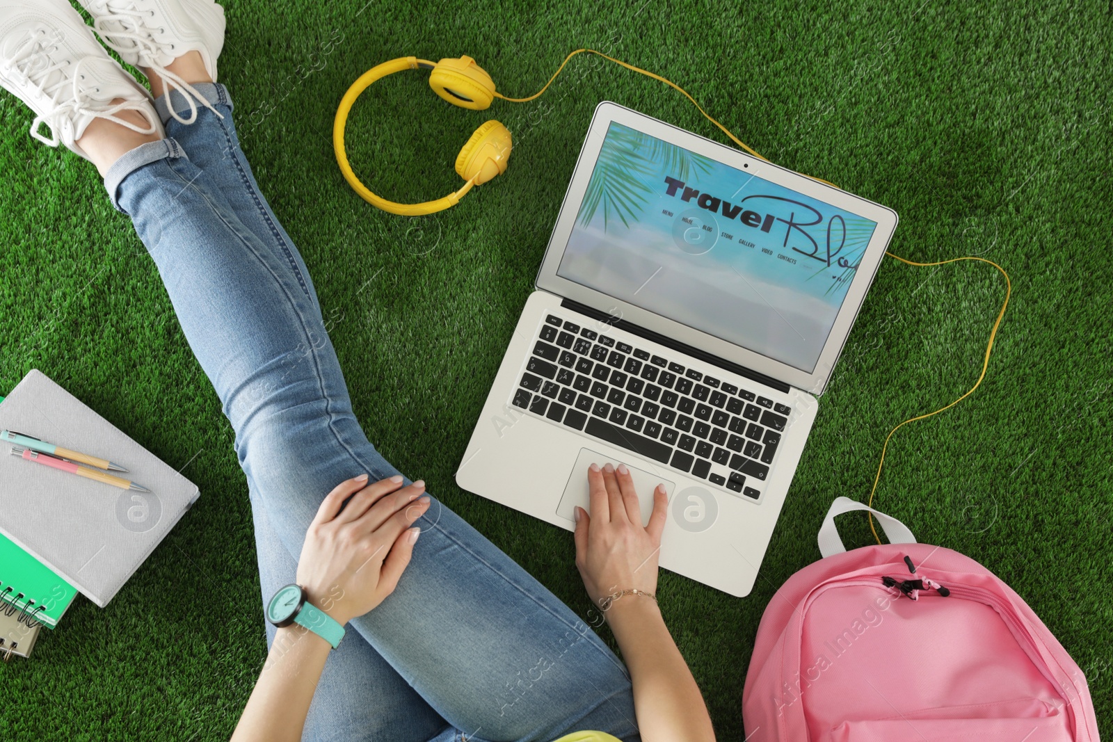 Photo of Woman and laptop with open travel blogger site on artificial grass, top view